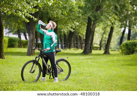 Man in track-suit with bicycle drinking water at summer park
