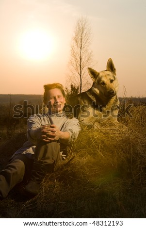 Woman with alsatian dog lying at haystack at sunset