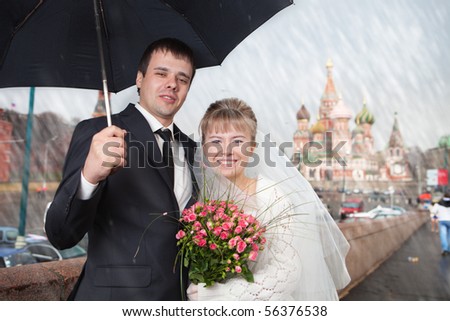 The newly married couple under the rain at Moscow near Kremlin. The Cathedral of the Virgin Protectress at background