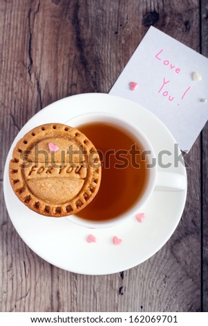 Homemade cookies with stamp: for you on cup of tea and white paper for a note text Love you