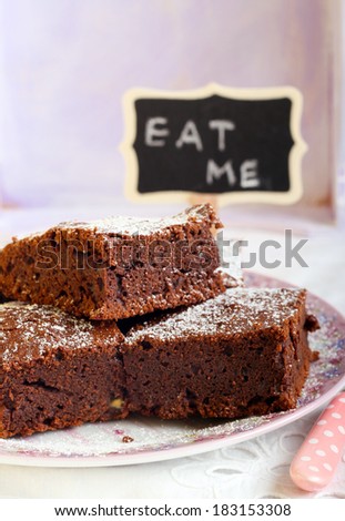 Chocolate brownies dusted with icing sugar on plate and a sign saying Eat me