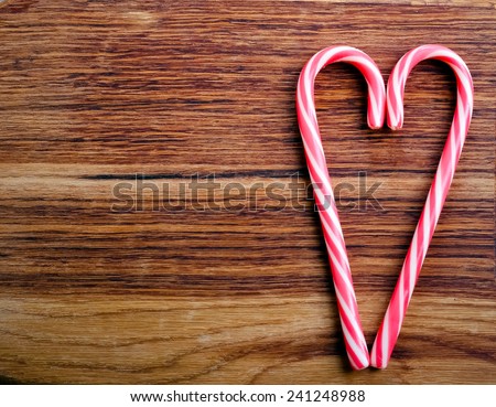 Two candy canes in heart shape over wooden surface