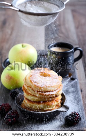 Dusting with icing sugar over apple fritters on a pan