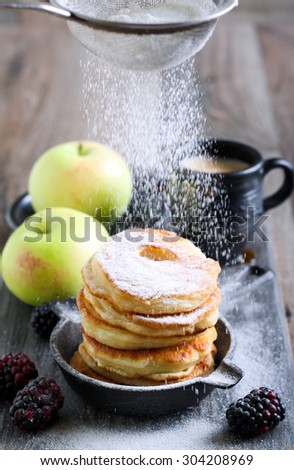 Dusting with icing sugar over apple fritters on a pan
