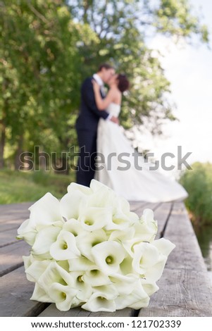 Wedding bouquet in focus in foreground, newlywed couple kissing out of focus in background