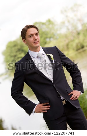 Elegant groom with self confident pose in front of a lake