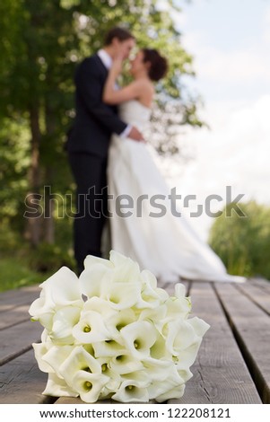 Wedding bouquet in focus in foreground, newlywed couple almost kissing out of focus in background