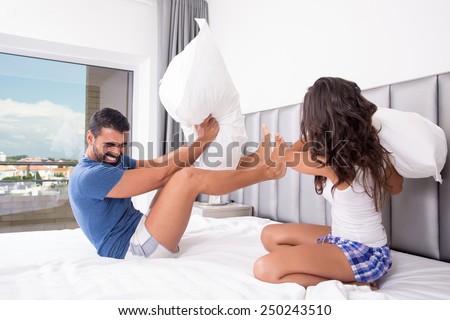 Funny couple fighting with pillows in bed