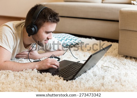 Man lying on the floor using headphones on laptop