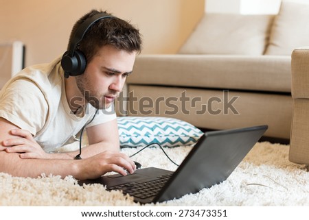 Man lying on the floor using headphones on laptop