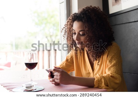 Afro woman typing on smartphone in restaurant