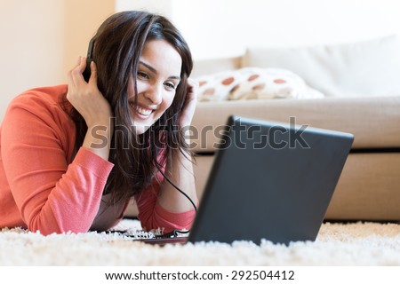 Woman lying on the floor using headphones on laptop