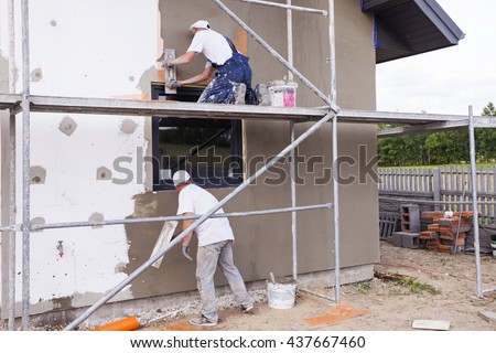 Workers spreading mortar over styrofoam insulation and mesh with trowel