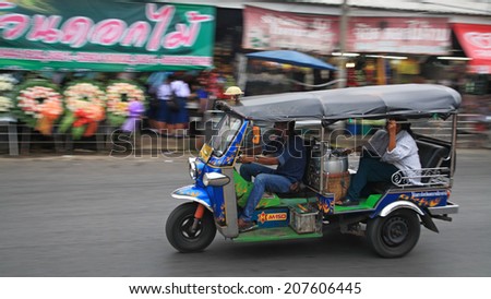 BANGKOK, THAILAND - JULY 18, 2014: Unidentified driver and passenger in tricycle called tuk tuk along street near fresh flower market. Tuk tuk is very good transmission for traffic jam in the city.
