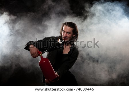 The young man in a black shirt extinguishes a burning cigarette. The man uses the red fire extinguisher. White smoke on a dark background.