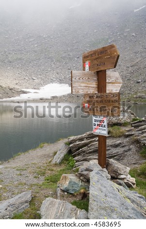 Pole with wooden direction signs and walking times for hikers in a mountain landscape in the Italian Alps.