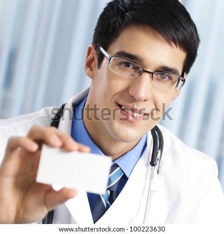 Portrait of happy smiling cheerful young doctor showing business card, at office