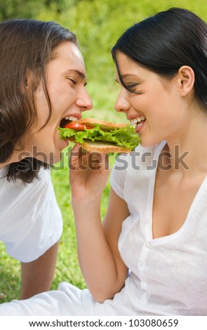 Young happy couple eating sandwich together outdoors