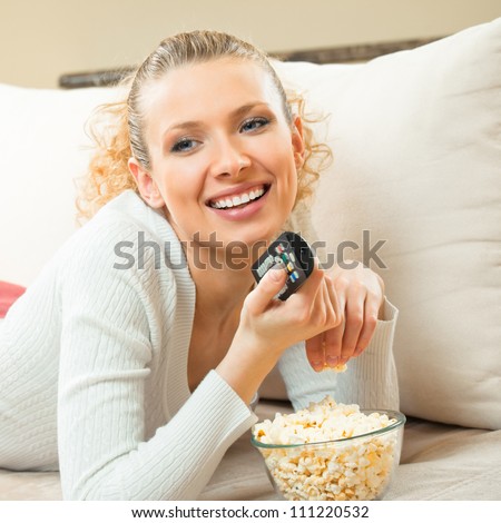 Portrait of young blond happy smiling woman watching TV at home