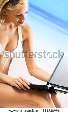 Young happy smiling woman with laptop, working, chatting, searching or walking by mobile internet on beach