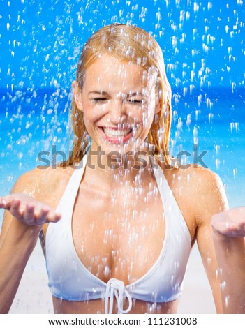 Young beautiful happy tanned blond woman in bikini at rain or summer shower on beach
