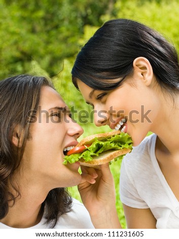 Young happy couple eating sandwich together outdoors