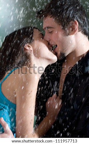 Young happy amorous couple hugging and kissing under a rain, outdoors