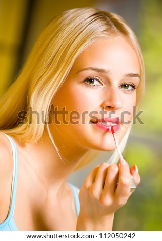 Portrait of happy young beautiful woman applying lipstick at home