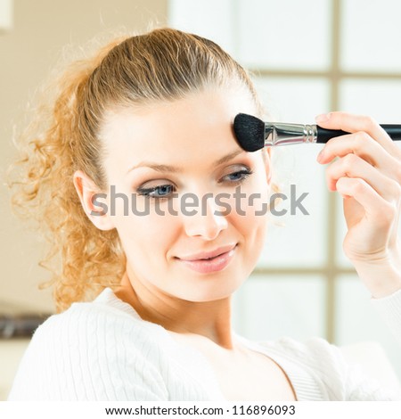 Cheerful smiling woman with mirror and makeup brush