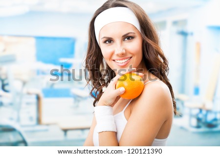 Cheerful young beautiful woman with orange, at fitness center or gym