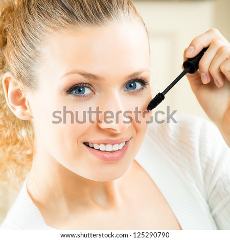 Cheerful woman applying mascara with lash brush