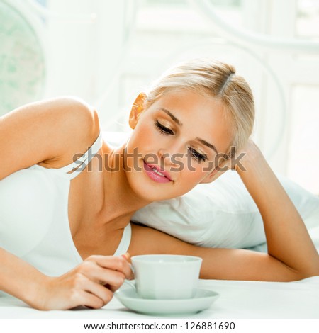 Happy smiling beautiful blond woman awaking with cup of coffee at bedroom