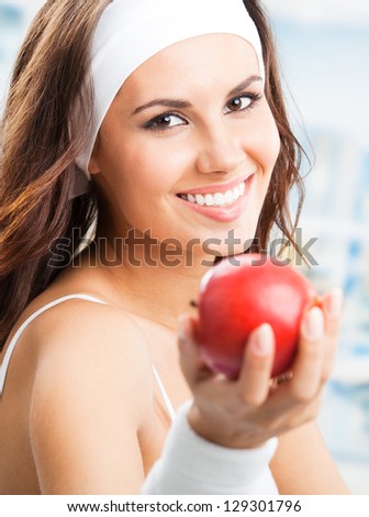 Cheerful young beautiful woman with red apple, at fitness center or gym