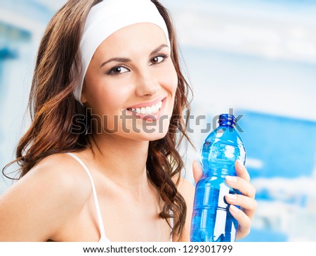 Portrait of cheerful young attractive woman with bottle of water, at fitness club or gym