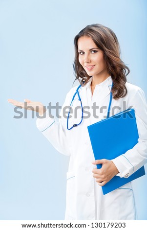 Portrait of young female doctor showing something or copyspase for product or sign text, with blue foder, over blue background
