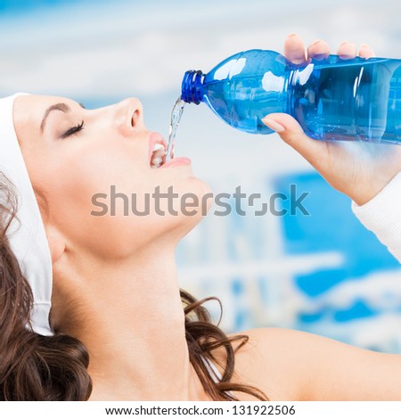 Portrait of cheerful young attractive woman drinking water, at fitness club or gym