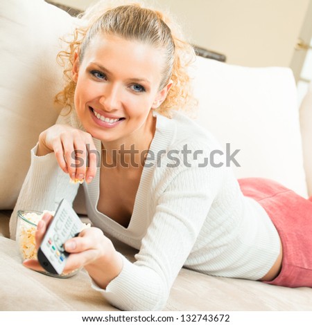 Portrait of young blond happy smiling woman watching TV at home