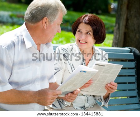 Happy smiling attractive senior couple reading together, outdoors