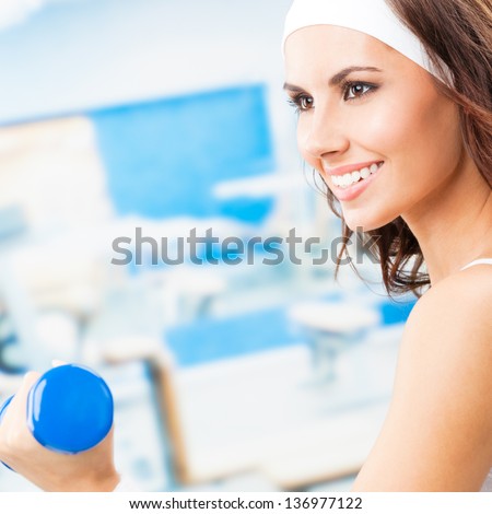 Cheerful woman in fitness wear exercising with dumbbell, at fitness center or gym, with copyspace