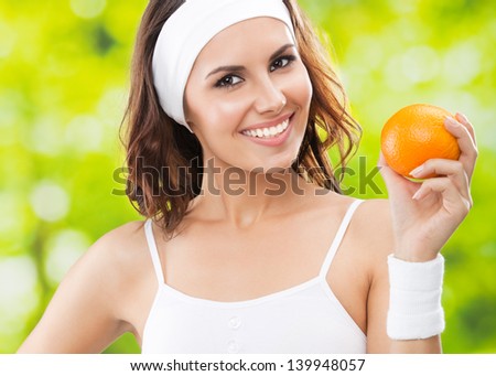 Portrait of happy smiling young beautiful woman in fitness wear with orange, outdoors
