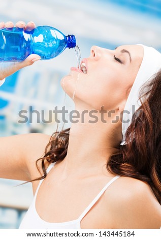 Portrait of cheerful young attractive woman  drinking water, at fitness club or gym