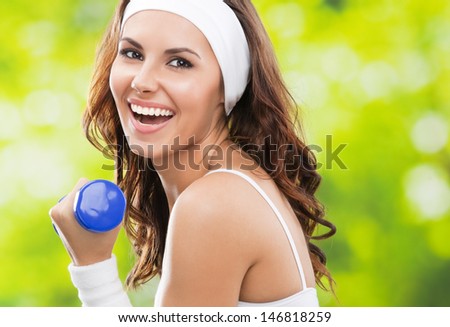 Portrait of cheerful woman in fitness wear exercising with dumbbell, outdoors, with copyspace