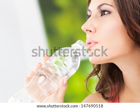 Portrait of young woman drinking water from bottle, outdoors, with copyspace