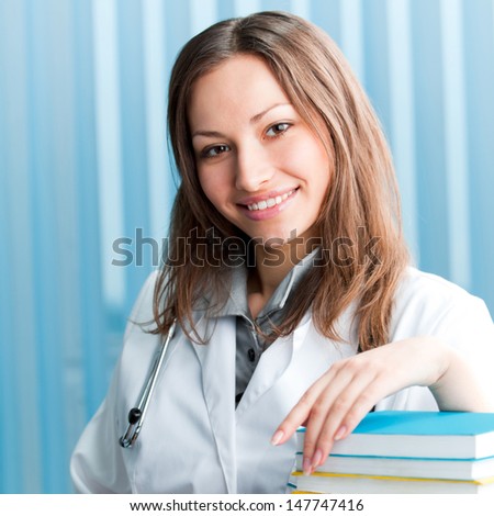 Portrait of cheerful female doctor with books at office