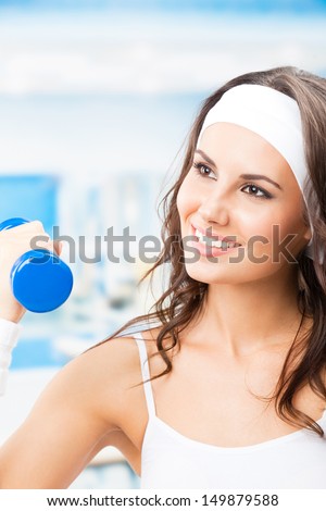 Cheerful woman in fitness wear exercising with dumbbell, at fitness center or gym