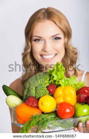Portrait of happy smiling young beautiful woman with healthy vegetarian raw food, over gray. Selective focus on food.
