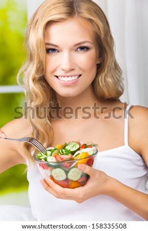 Portrait of happy smiling young woman with vegetarian vegetable salad, indoors