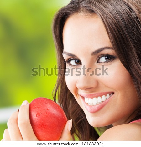 Portrait of young woman with red apple, outdoors