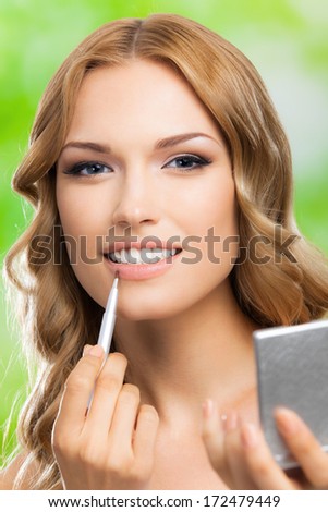 Portrait of young happy smiling woman with make up brush and mirror, outdoors