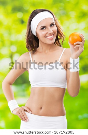 Portrait of happy smiling young beautiful woman in fitness wear with orange, outdoors